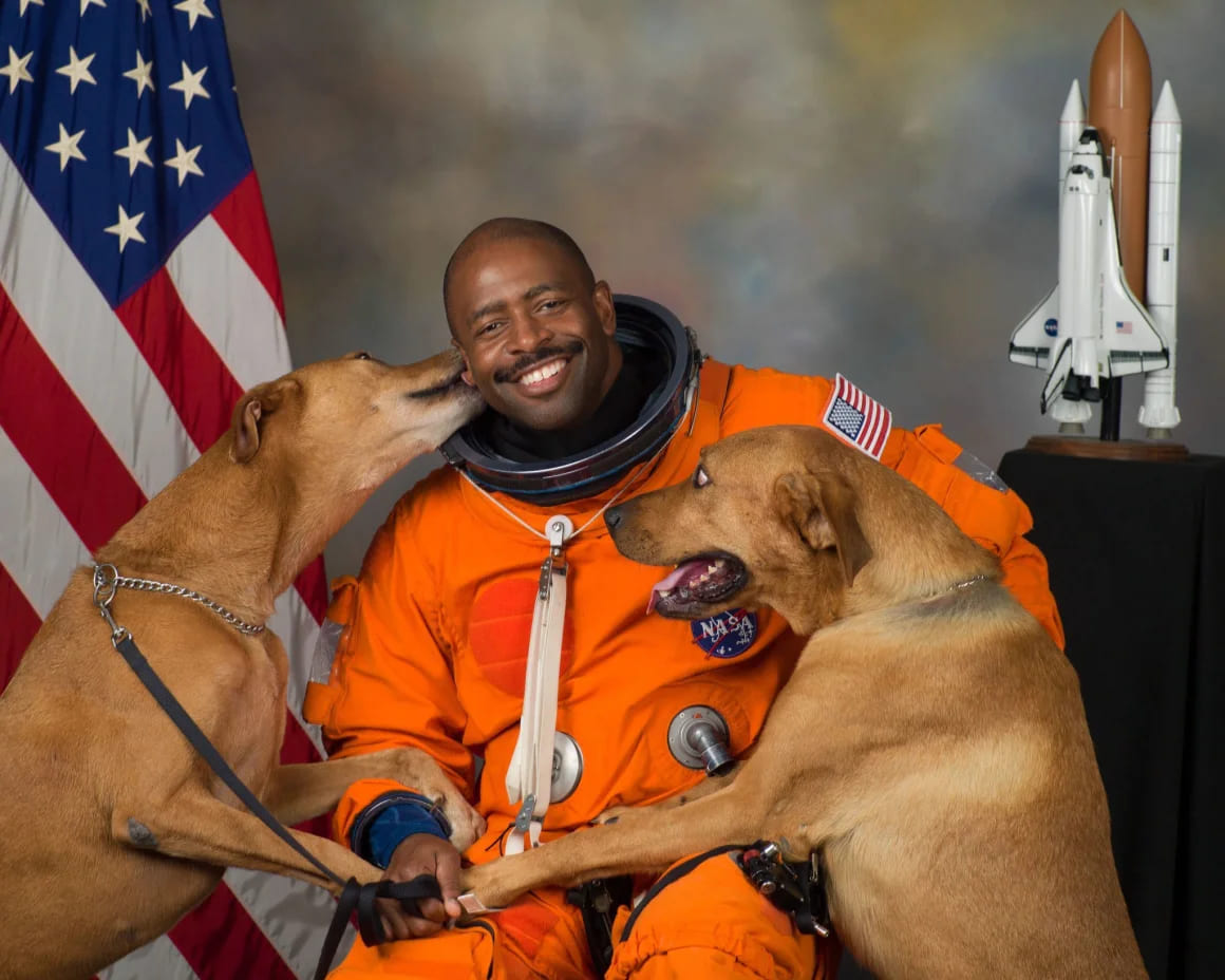 NASA astronaut Leland Melvin official portrait with rescue dogs Jake and Scout sitting beside him in orange flight suit